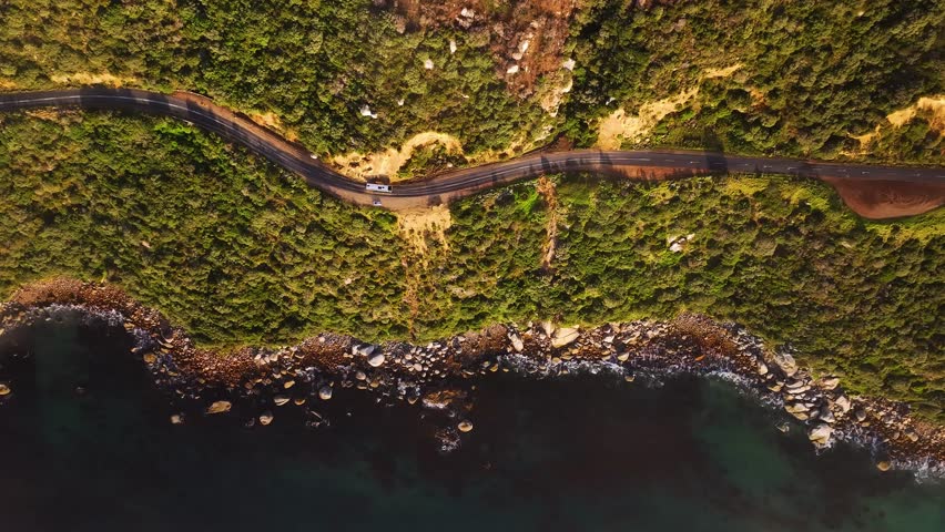 Aerial view of coastal road winding beside the rocky shoreline contrasting the ocean