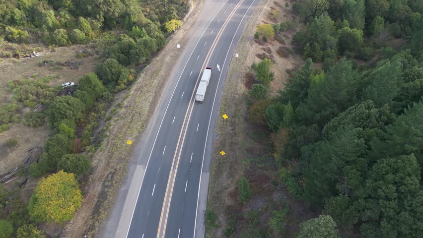 Aerial view of trucks on a bridge over a shallow river surrounded by lush green trees and autumnal grasslands, Benbow, California, United States.