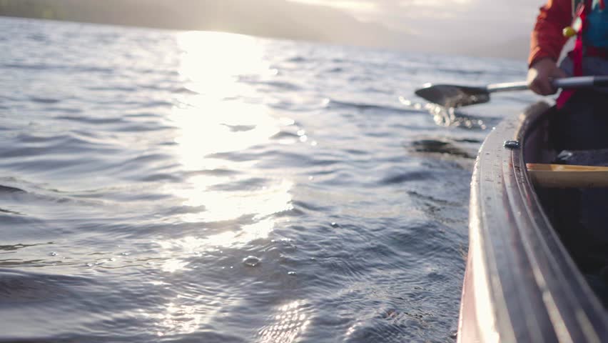 Lone canoe paddler moving across still water on a remote loch in Scotland