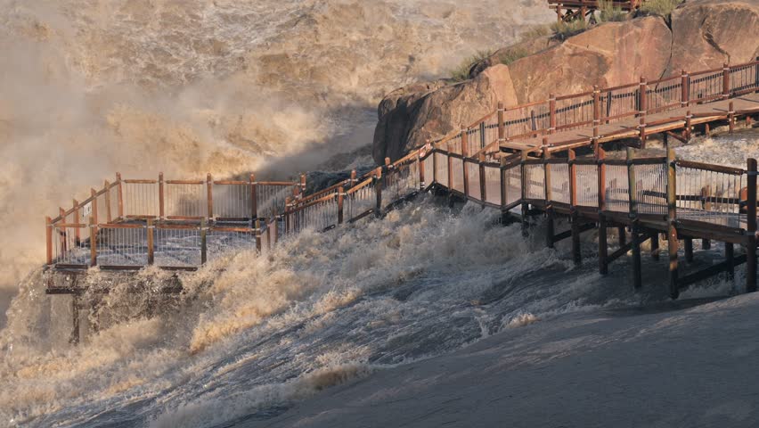 Water flows across viewing deck and walkway by Augrabies main waterfall, Orange River in flood
