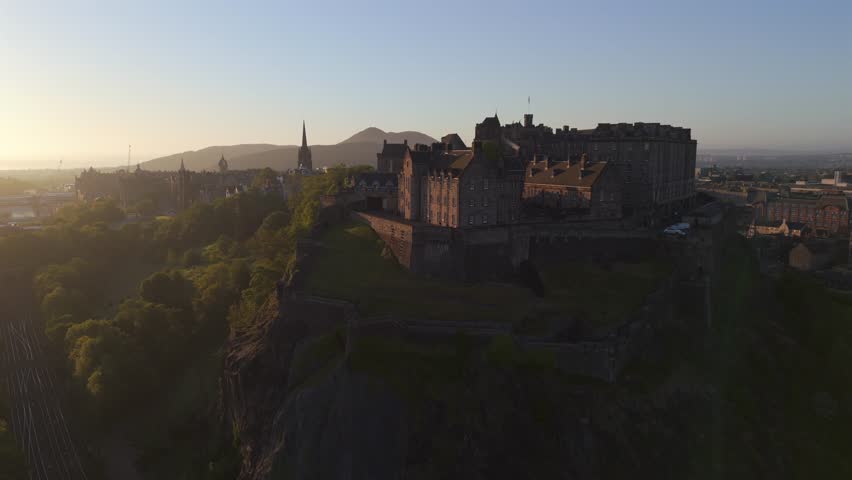 Aerial view of Edinburgh Castle atop a craggy peak, the sun casting a golden glow on the city