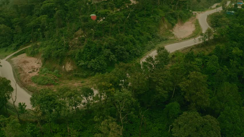 Aerial view of a winding road cutting through lush green trees, with a car moving along the road, Sakleshpura, Karnataka, India.