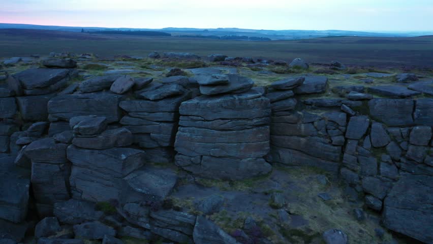 Aerial view of dramatic rock formations, with rugged textures and muted tones, under a soft, dusky sky, Hope Valley, England, United Kingdom.
