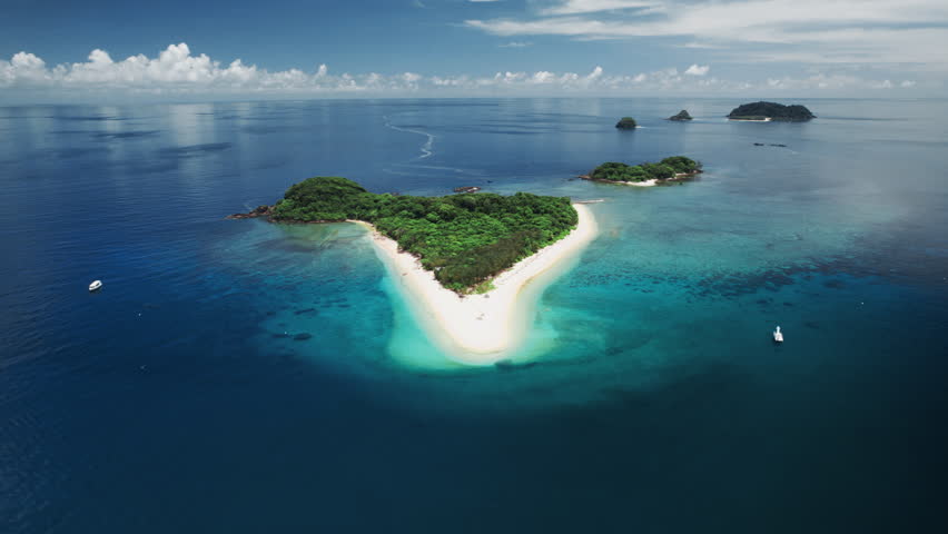 Drone pull-back shot revealing a tropical island, shallow reef lagoon, and surrounding coral reef at Frankland Islands in the Great Barrier Reef.
