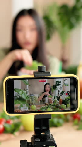 A young woman records herself preparing a healthy meal with fresh ingredients, showcasing a modern approach to content creation and healthy living