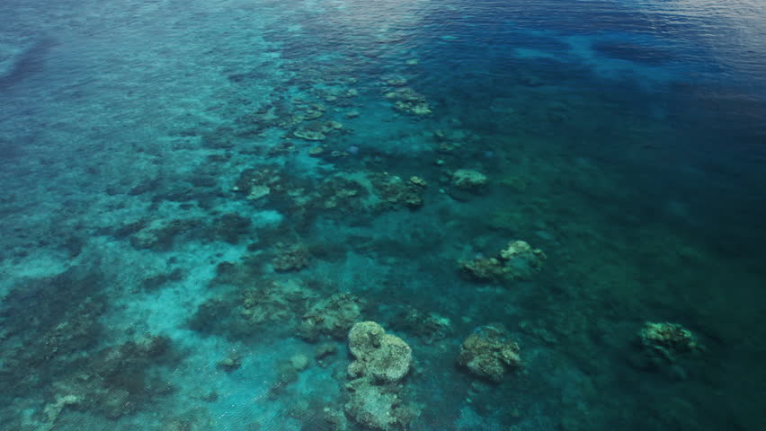 Drone push-in aerial shot flying over shallow coral reef toward Frankland Island, surrounded by clear turquoise water in the Great Barrier Reef