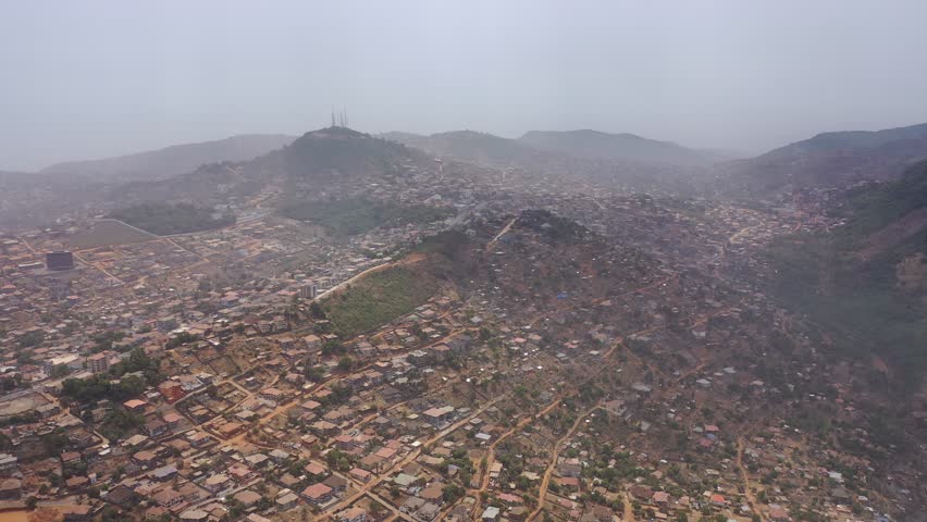 Aerial view of densely populated housing cascading down hillsides, and a mountain with antennas, a contrast of urban sprawl and natural landscape, Freetown, Sierra Leone.