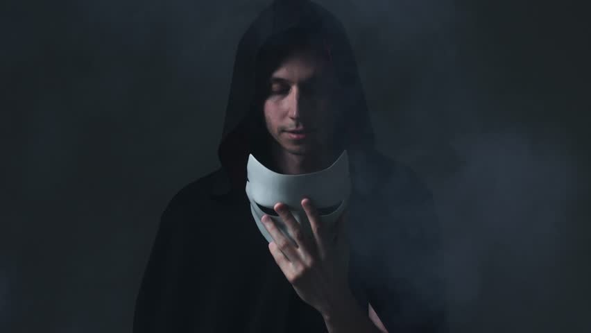 A figure in a mystical black cloak with a raised hood completes his transformation by donning a mask, embodying the concept of becoming an anonymous, secret member.