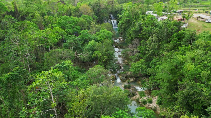 Cinematic forward-closing-in aerial shot approaching the multi-tiered cascades of Bolinao Falls in Pangasinan, Philippines, focusing on the powerful white water rushing into the water below.