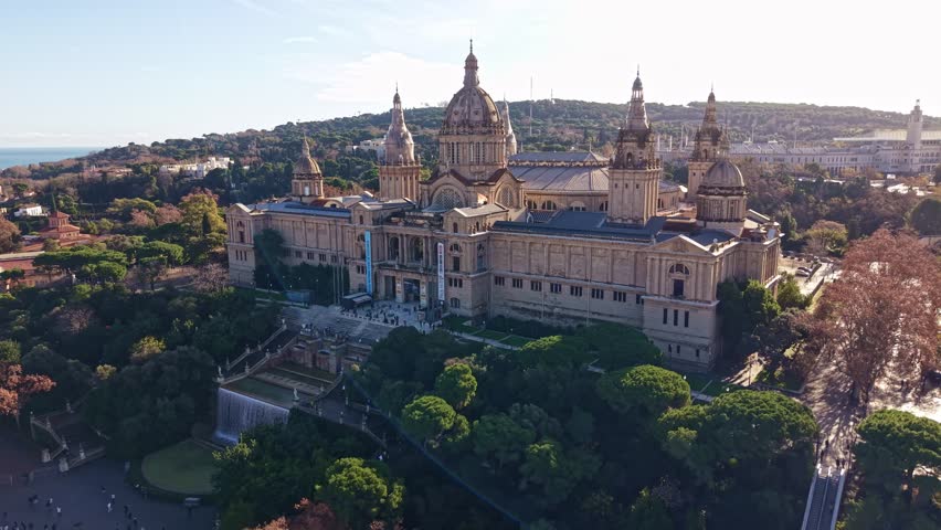 Palau Nacional, National Palace on Montjuïc hill, home to the National Art Museum of Catalonia (MNAC), illuminated by the warm light of a sunny day in Barcelona, Spain. Aerial backward