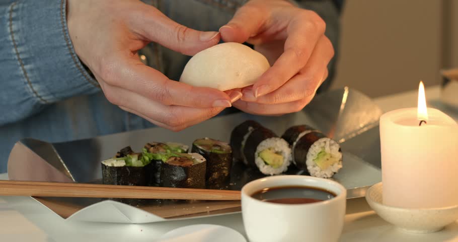 Hands taking mochi on the background of a box of takeaway sushi rolls.