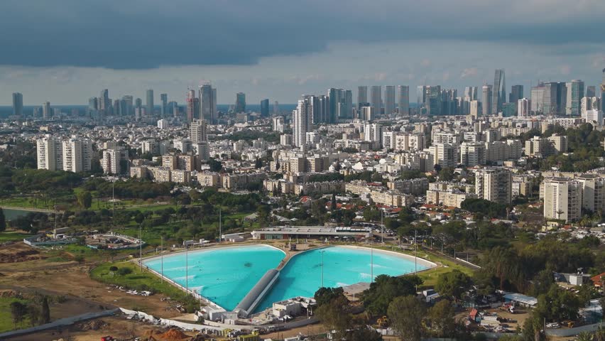 Surfing lagoon in South Tel Aviv with the city's old neighborhoods and modern skyscrapers visible in the background.