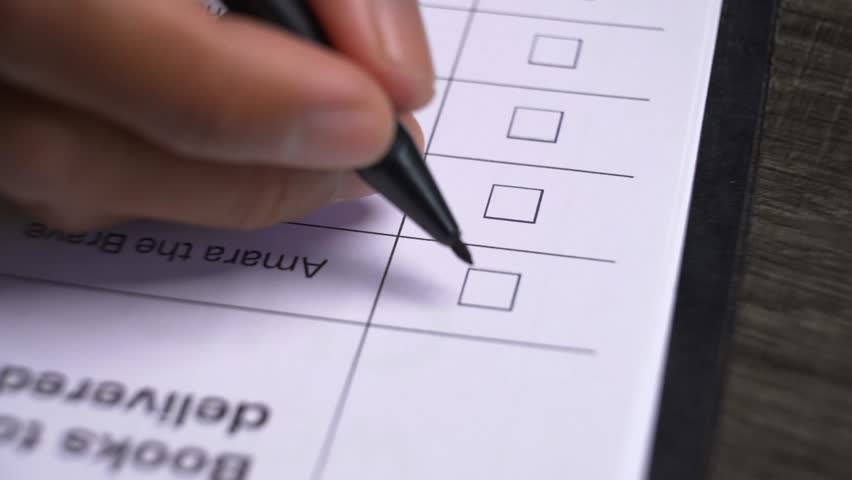 Close up view of a person's hand with a pen marking or ticking multiple checkboxes on a document or survey form