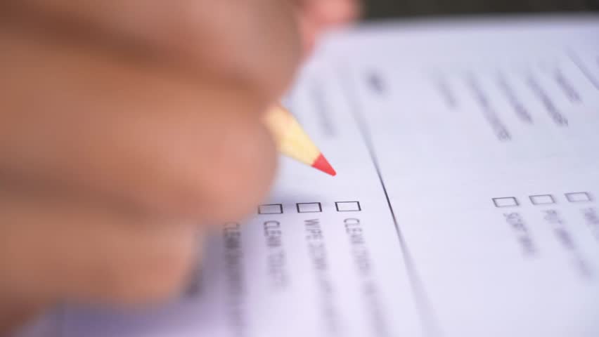 Person's hand marking a series of checkboxes on a document or form with a pencil during a task