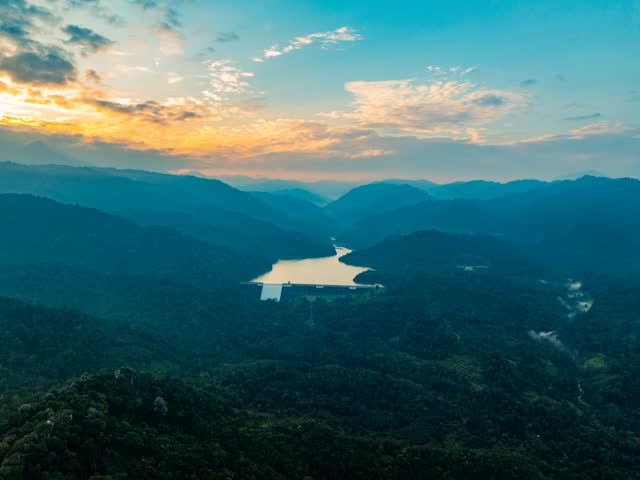 Aerial view of dam reservoir surrounded by lush tropical rainforest and mountains under dramatic cloudy sky. 4k resolution hyperlapse video.