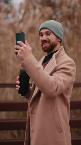 Smiling Man Capturing a Moment with His Smartphone and Coffee Mug in a Park