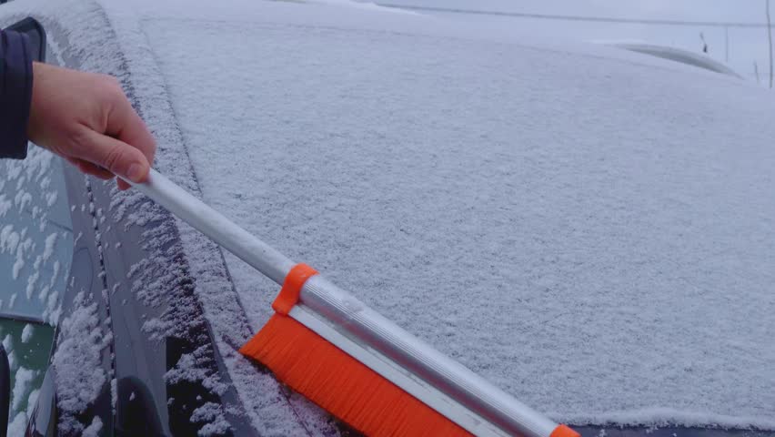 Winter morning. Removing frost from car windshield with orange snow brush.