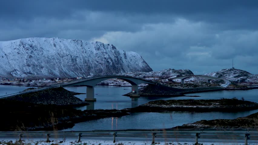 The iconic curved Fredvang Bridges at twilight with snow-capped mountains in Lofoten, Norway.Blue hour at Fredvang, Norway, featuring the famous bridge architecture and arctic mountain landscape.
