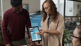Handheld zoom out shot of group of four diverse designers using digital tablet and laptop to discuss ideas during meeting in bureau - Powered by Shutterstock - Get 15% off with code: PIKWIZARD15