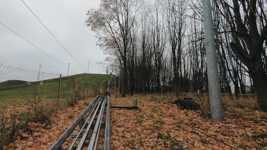Narrow railway track running uphill through an autumn landscape with bare trees and fallen leaves, overcast sky, rural outdoor environment, infrastructure integrated into nature, no people