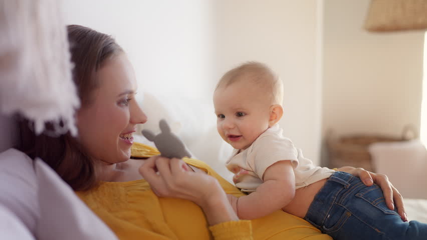 Cheerful woman playing with adorable baby girl, showing soft textile toy