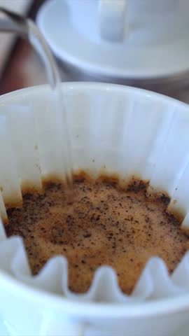 Close up of hot water being poured into a paper filter with fresh ground coffee for a pour over brew, showing the blooming process and extraction in a white ceramic dripper
