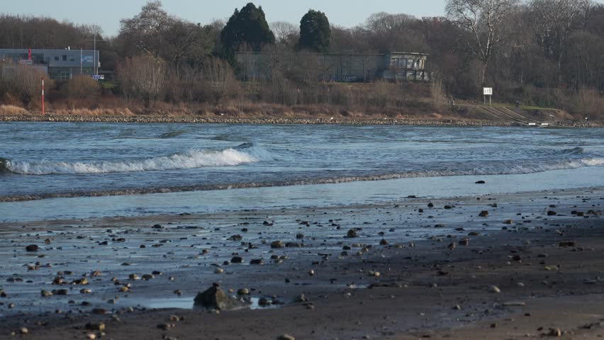 Detailed view of a muddy and rocky riverbank with sparkling water surface.