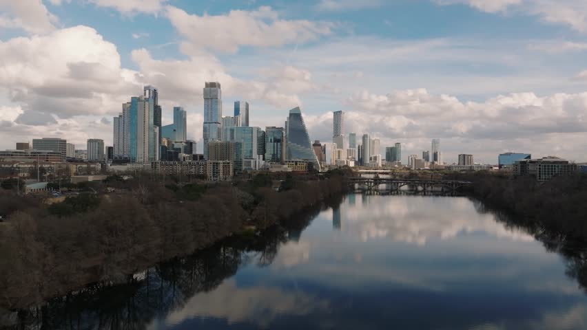 Aerial drone flying along the Colorado River towards the skyline of Austin Texas on a winter afternoon with very calm water reflecting the cityscape