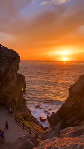 4K Vertical cinematic golden sunset over the Strait of Gibraltar from Dalia beach, Tangier. Stunning rocks and ocean waves with a vibrant orange sky in Morocco.