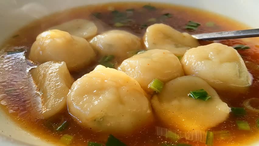 Footage of delicious homemade Asian fish ball soup with savory broth and fresh scallions in a hot white bowl.