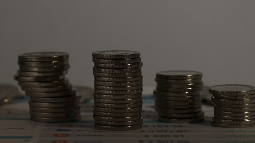 Stacks of coins on wooden table against grey background, closeup. Changing direction of light