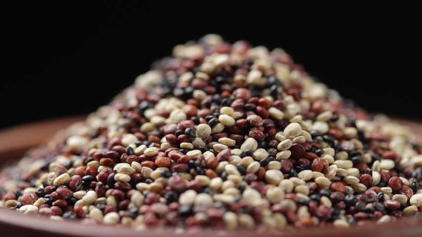Mix of white, red, and black quinoa seeds in brown wooden bowl rotating slowly on balck background, Close-up view