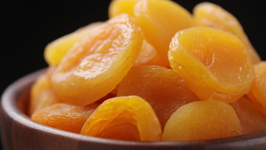 Pile of dried apricots fruit in brown wooden bowl rotating slowly on balck background, Close-up view