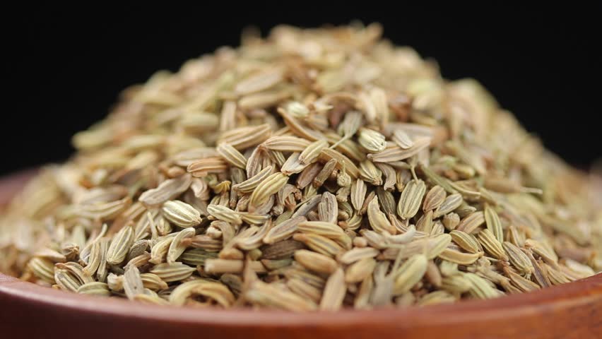Pile of fennel seeds in brown wooden bowl rotating slowly on balck background, Close-up view