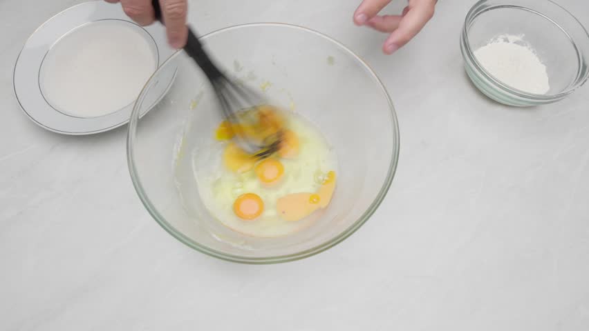 Hands whisking eggs in a glass bowl during cake preparation.