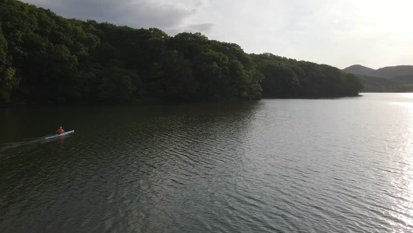 View from above. An athlete trains on a kayak on a lake among green hills. Kayaker training.