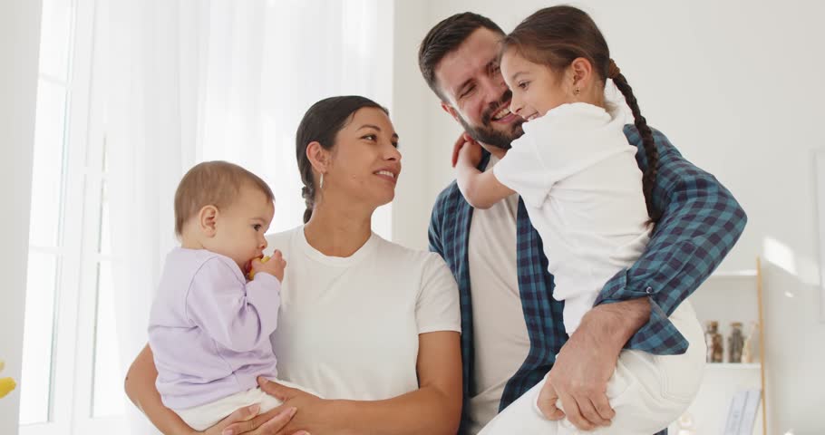 Family parents children smiling together at home. Parents hold a baby and a daughter, sharing warmth and love in a bright room. Happiness and unity indoors. Concept: family portrait at home.