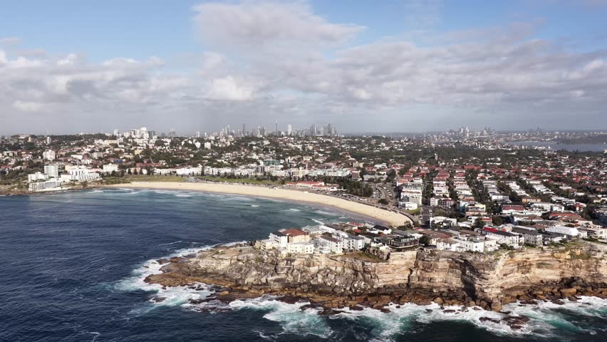 Zoom in to Bondi Beach and Sydney city CBD on horizon – landmark destinations of Australia.
