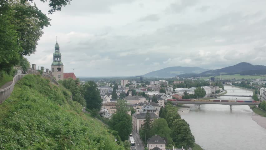 Cinematic dolly out view of historic Salzburg city buildings and riverbank under overcast sky.