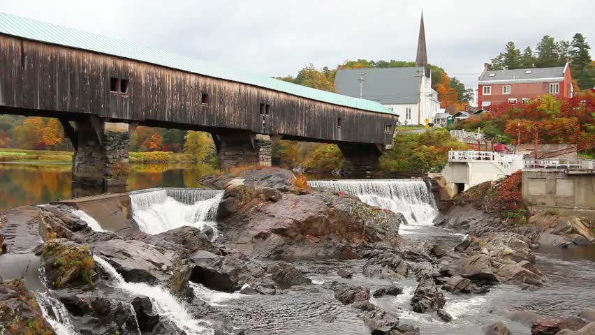 A scenic covered bridge in Stowe, Vermont, with a waterfall and vibrant fall foliage, creating a picturesque autumn landscape.