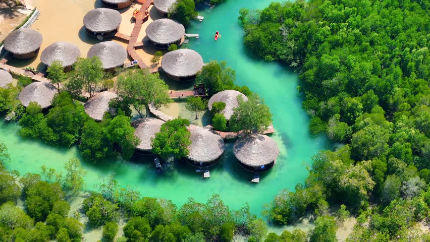 Aerial drone view of bungalows surrounded by mangroves and turquoise lagoon waters on Koh Phayam, Thailand.