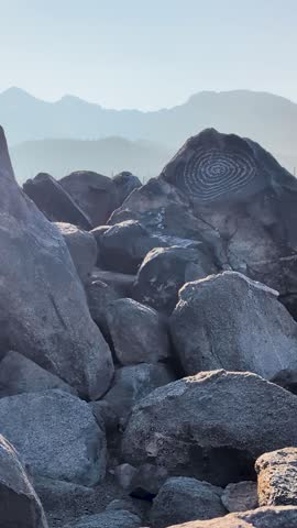 Vertical footage of an ancient spiral petroglyph carved into desert rock at Signal Hill in Saguaro National Park. Soft sunrise light, layered stones, and a quiet, timeless desert atmosphere.