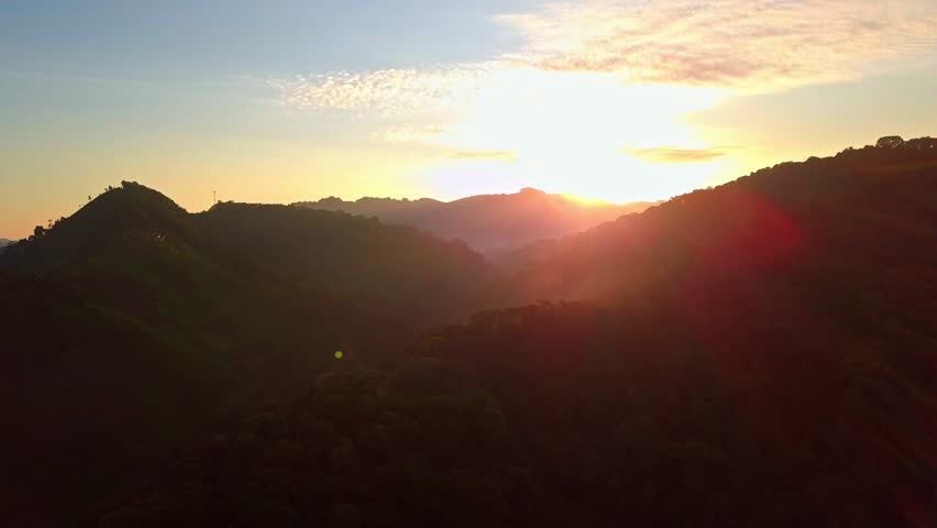 Sunset over rolling hills and deep valleys of Rubanda District, Uganda, bathing lush tea plantations and forested slopes in warm golden light, a serene agricultural panorama, aerial