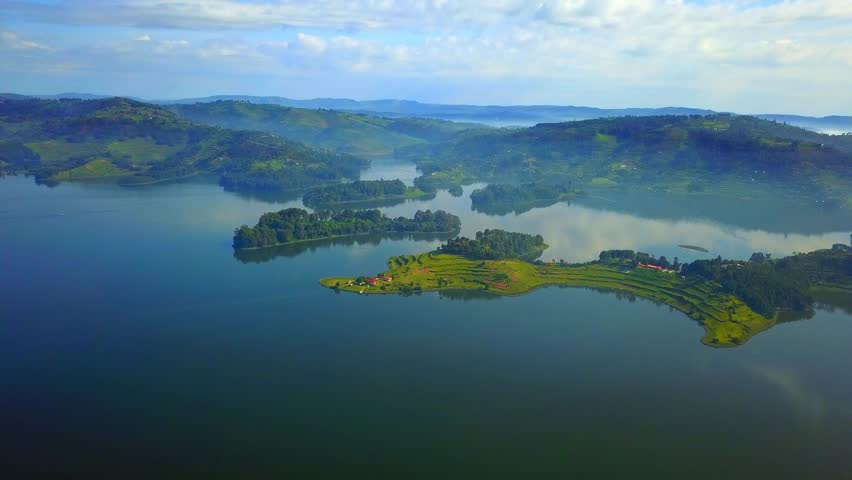 Lake Bunyonyi, Uganda, from above, showing numerous green islands and terraced hillsides emerging from the calm water, reflecting the sky, creating a peaceful African landscape