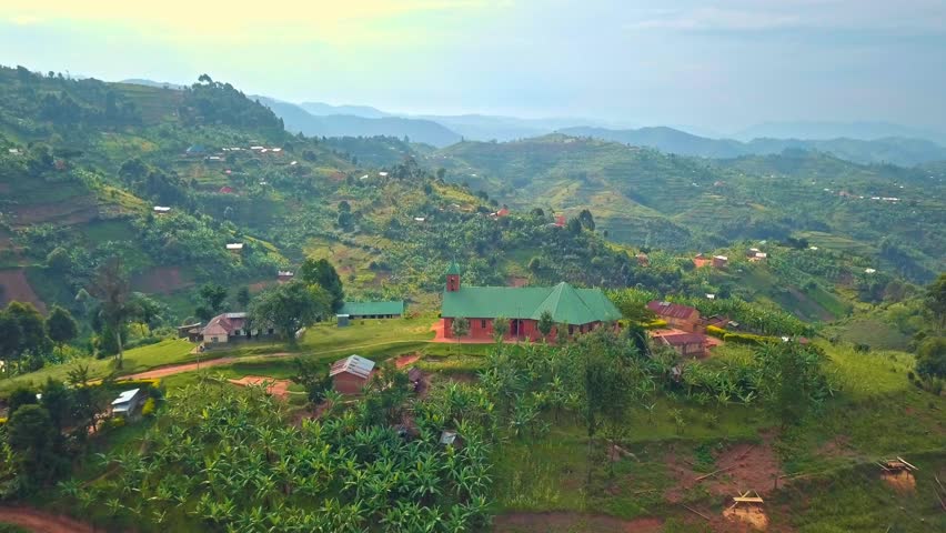 Drone glides over Rural community life in Uganda's Rubanda District with a prominent church and clustered homes amid terraced tea plantations and lush green hills under clear daytime skies
