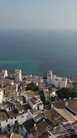 Vertical aerial pullback revealing the iconic dome of the Nuestra Señora del Consuelo Church rising above the coastal cityscape of Altea, Spain.