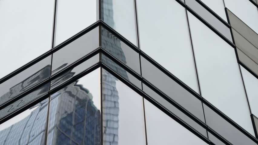 Angular glass facade of a modern office building capturing distorted reflections of a neighboring skyscraper, emphasizing geometric lines, mirrored surfaces, and urban symmetry
