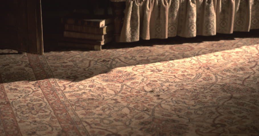 Men's black vintage shoes walk over an old carpet toward a wooden box, camera pan, 1950s style.