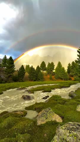 Magical double rainbow over a rushing mountain river and pine forest in a breathtaking green valley.
