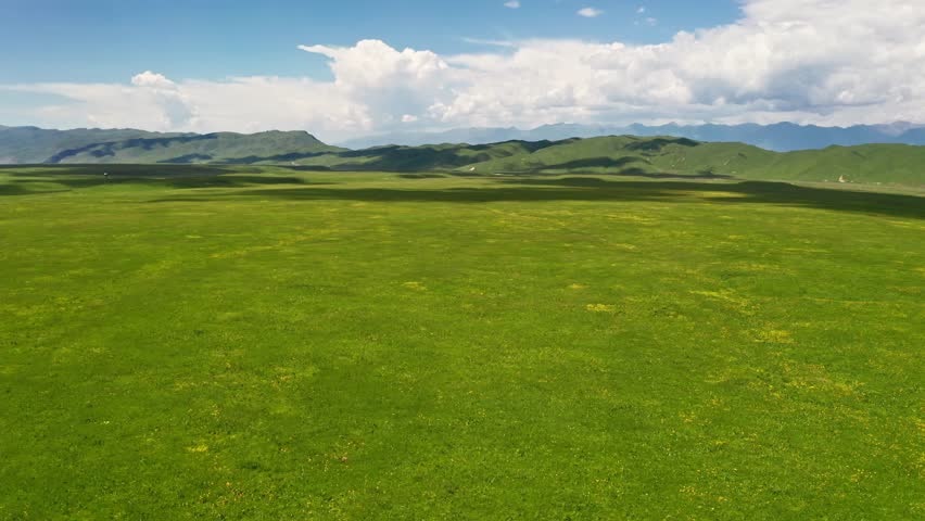 Aerial view vast green mountain prairie with moving clouds shadows under a clear blue sky, a stunning natural landscape